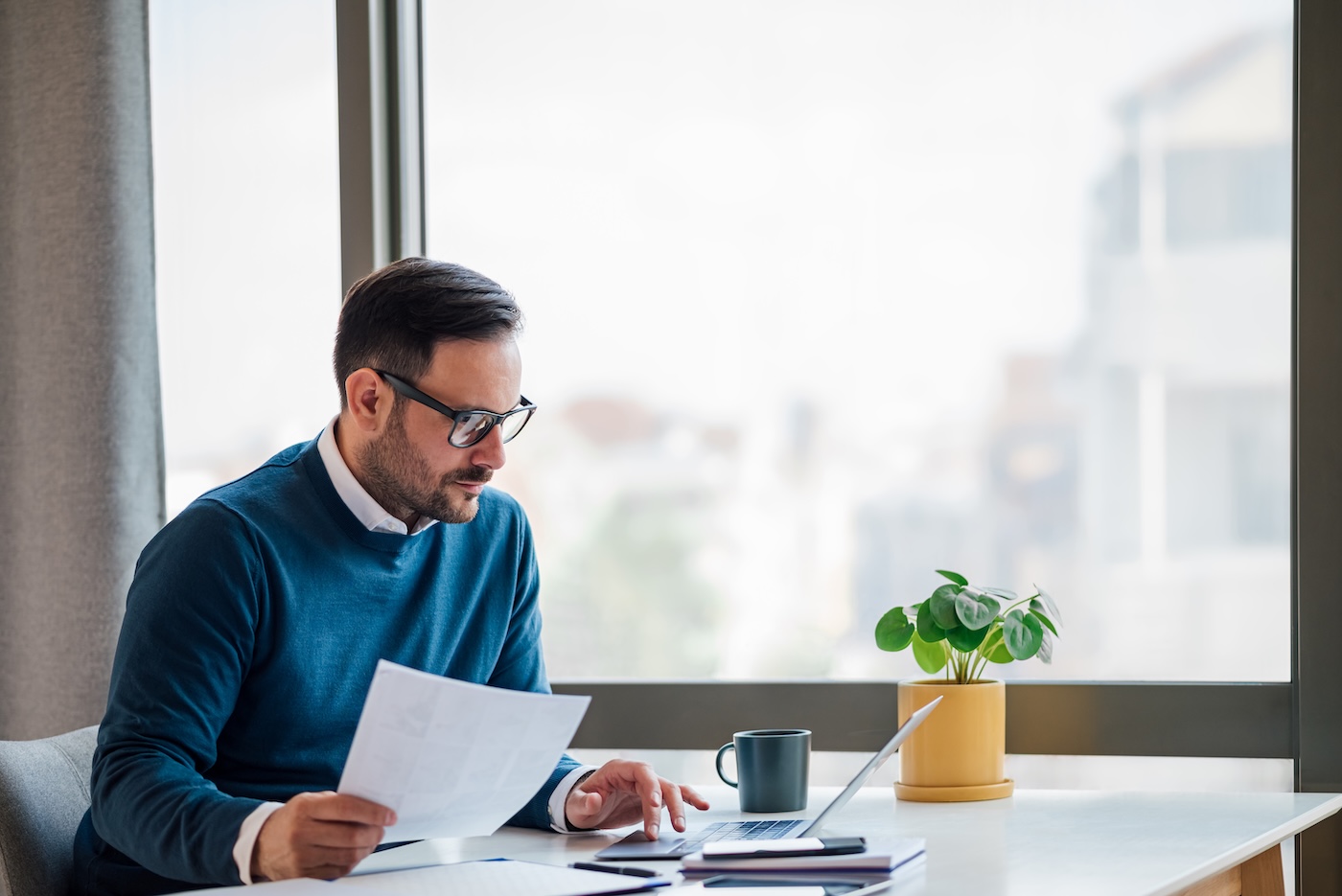 Focused adult man with eyeglasses, reviewing the job application of an employee.
